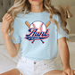 A woman wearing a light blue t-shirt with a graphic design of a baseball bat and ball, along with the text "Aunt of the Rookie".