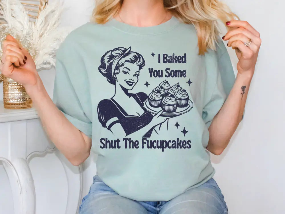 a woman holding a plate of cupcakes wearing a t - shirt