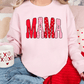 A woman wearing a pink sweatshirt with the word "MAMA" printed on it, sitting on a couch with a coffee mug in her hand.