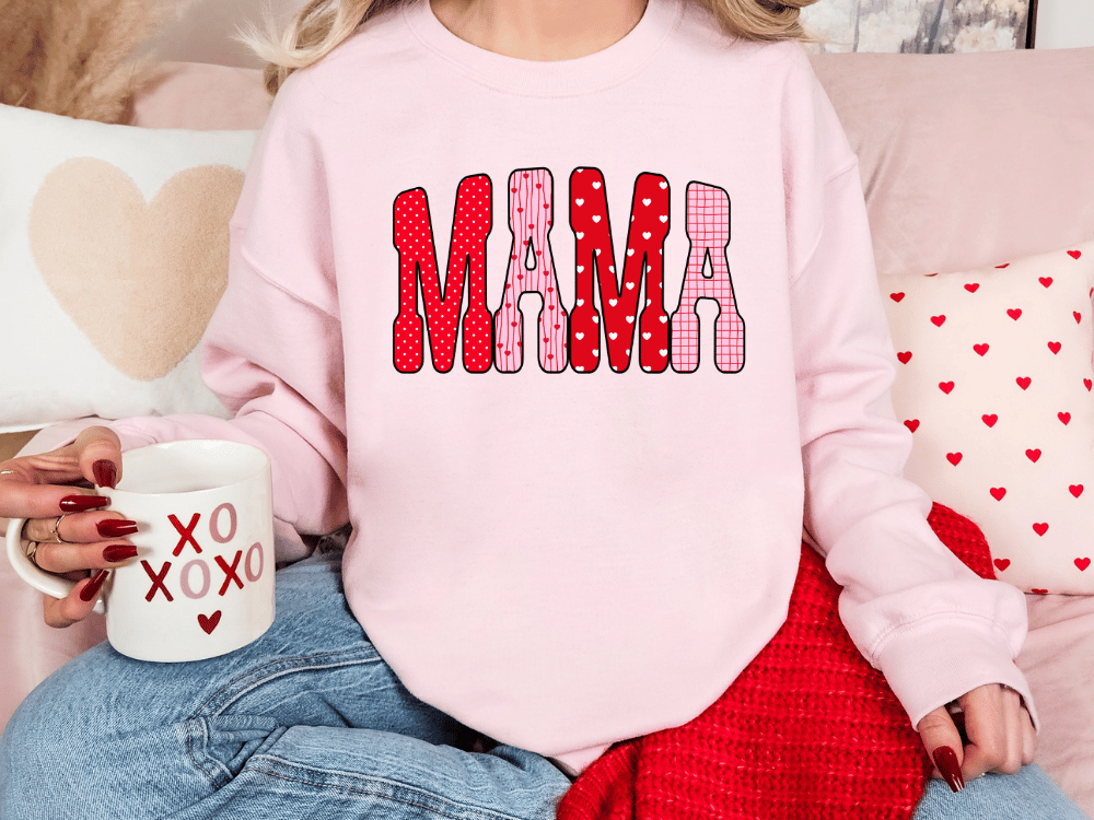 A woman wearing a pink sweatshirt with the word "MAMA" printed on it, sitting on a couch with a coffee mug in her hand.