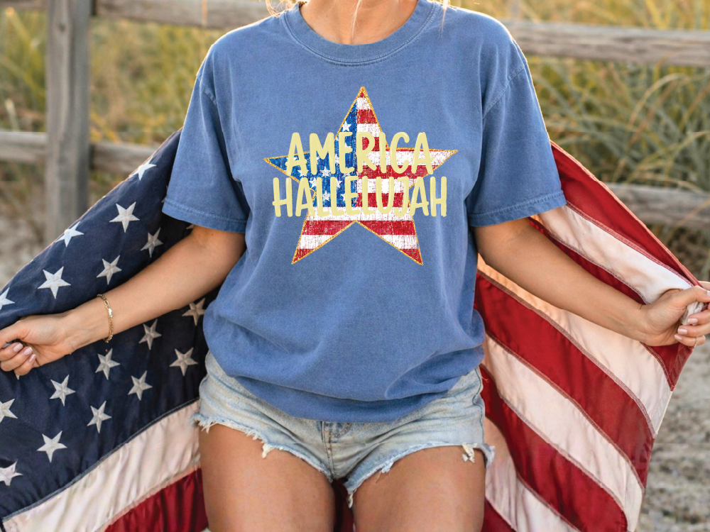 A person wearing a blue t-shirt with a star design and the text "AMERICA HALLOWEAH" is holding an American flag.