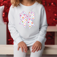 a little girl sitting on a bench with a bow on her shirt