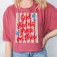 A woman wearing a red t-shirt with a patriotic design and text printed on it.