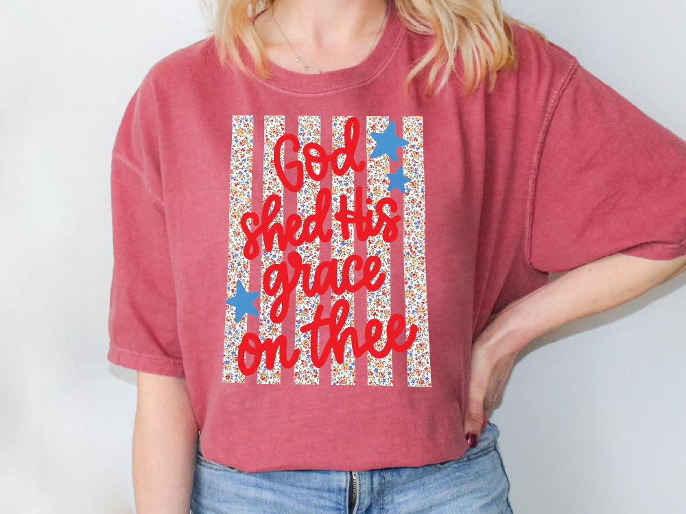 A woman wearing a red t-shirt with a patriotic design and text printed on it.