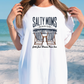 a woman standing on a beach wearing a white shirt