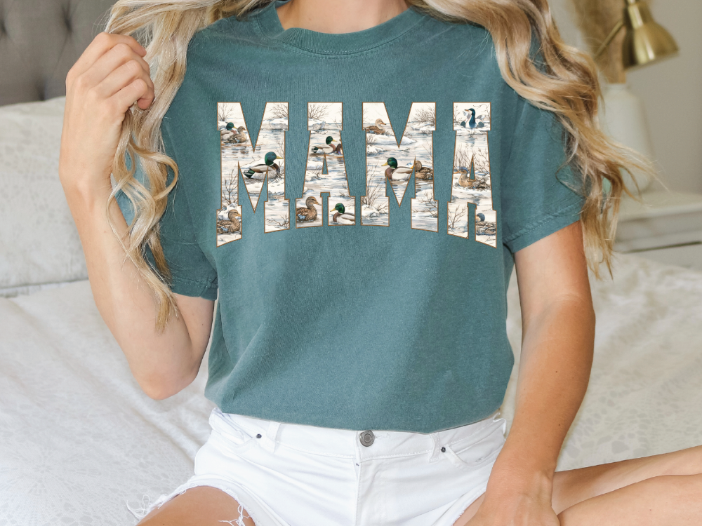 A woman wearing a green t-shirt with the word "MAMA" printed on it, sitting on a bed.