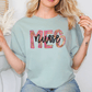A woman wearing a light blue t-shirt with the word "NURSE" printed on it, posing with her hands behind her back.