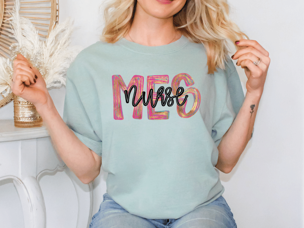 A woman wearing a light blue t-shirt with the word "NURSE" printed on it, posing with her hands behind her back.