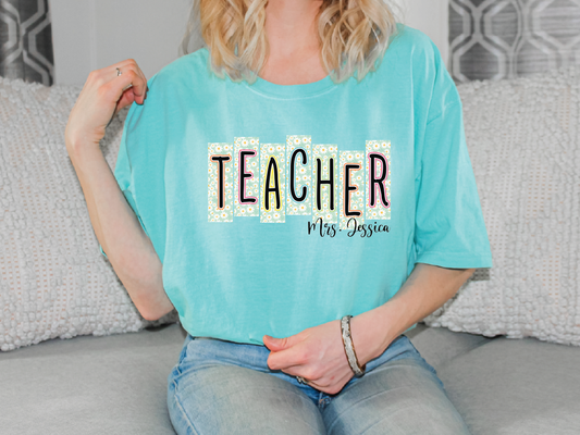 A woman wearing a teal t-shirt with the word "TEACHER" printed on it, sitting on a couch.
