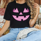 A woman wearing a black t-shirt with a pink jack-o-lantern graphic is sitting on a couch surrounded by fall decorations.