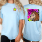 two women wearing light blue t-shirts with colorful designs. The t-shirt on the left has a star and a graphic of a unicorn, while the t-shirt on the right features a graphic of a horse with a checkered pattern and the word "Corns" written on it.