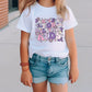 a little girl standing on a sidewalk wearing a white shirt