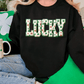 A person wearing a black sweatshirt with the word "Lucky" printed on it, sitting on a couch with a shamrock-themed mug and a green pillow.