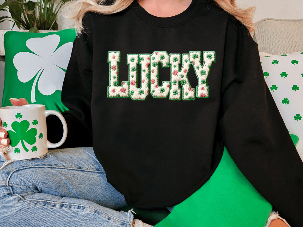 A person wearing a black sweatshirt with the word "Lucky" printed on it, sitting on a couch with a shamrock-themed mug and a green pillow.
