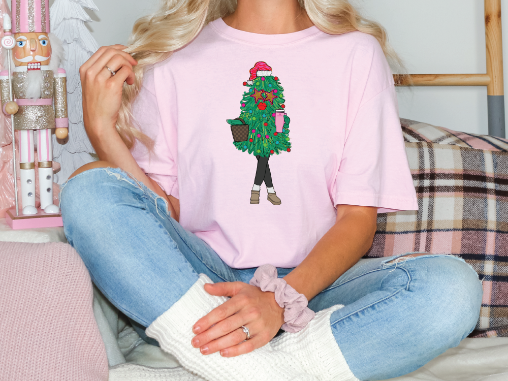 a woman sitting on a couch wearing a pink shirt with a christmas tree on it