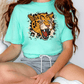 A person wearing a turquoise t-shirt with a graphic of a roaring leopard and gray shorts, sitting on the floor with their legs crossed.