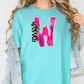 A woman wearing a turquoise t-shirt with a pink and black graphic design on it, and a denim jacket.