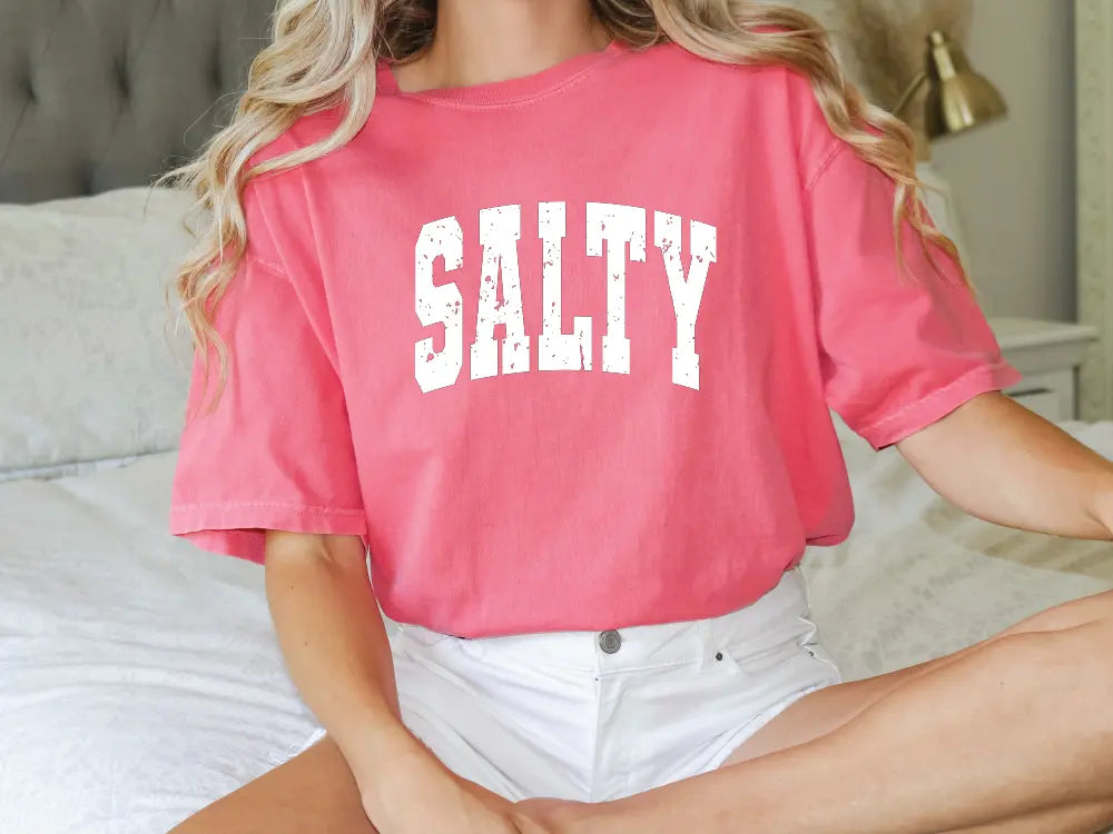 a woman sitting on a bed wearing a pink shirt