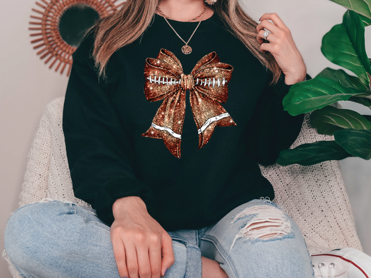 a woman sitting on a couch wearing a black sweatshirt with a gold bow