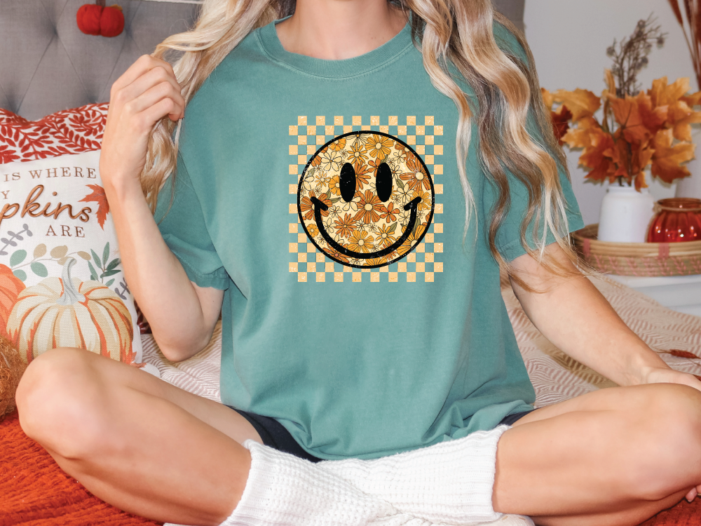 a woman sitting on a bed wearing a t - shirt with a smiley face on