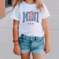 a little girl standing on a sidewalk wearing a t - shirt with an american flag