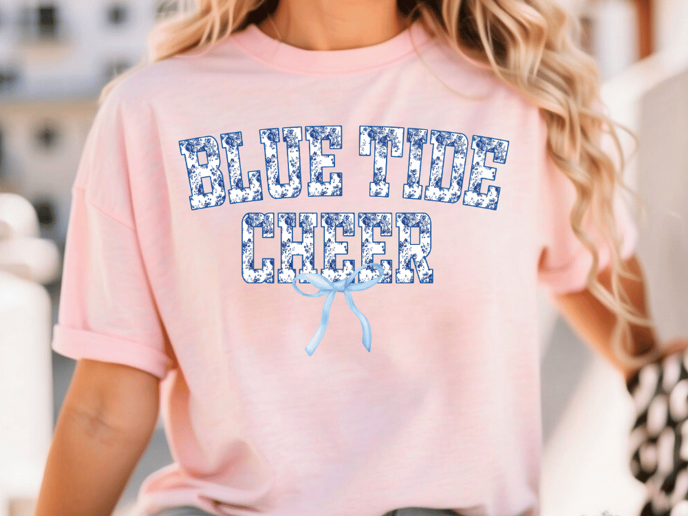A woman wearing a pink t-shirt with the text "BLUE TIDE CHEER" printed on it.