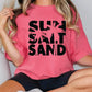 a woman wearing a pink shirt that says sun sand