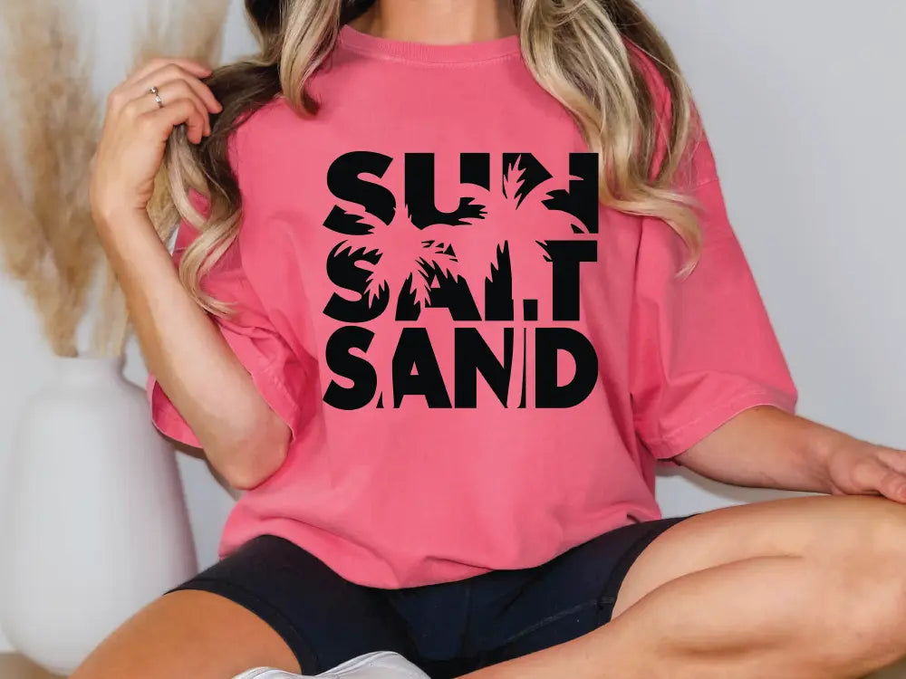 a woman wearing a pink shirt that says sun sand