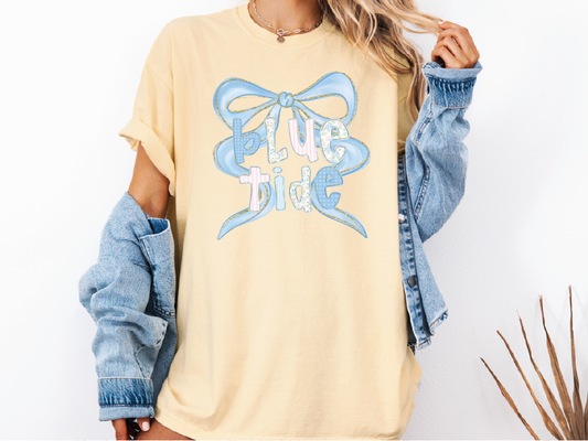 A woman wearing a yellow t-shirt with a blue bow and the text "Blue Tide" printed on it, along with a denim jacket.