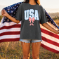 A person stands in a field holding an American flag, wearing a grey t-shirt with the word "USA" printed on it.