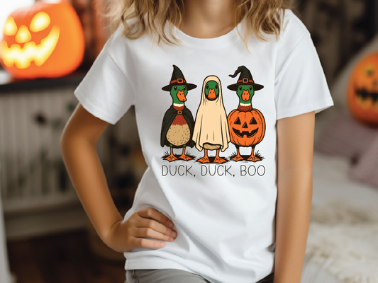 A white t-shirt with a graphic design featuring three cartoon ducks dressed in Halloween costumes, including a witch's hat, a pumpkin, and a ghost.