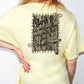 A person wearing a yellow t-shirt with a graphic design on the back, featuring a Bible verse and a wooden door.