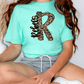 A person wearing a mint green t-shirt with a leopard print design and gray shorts is sitting on the floor.