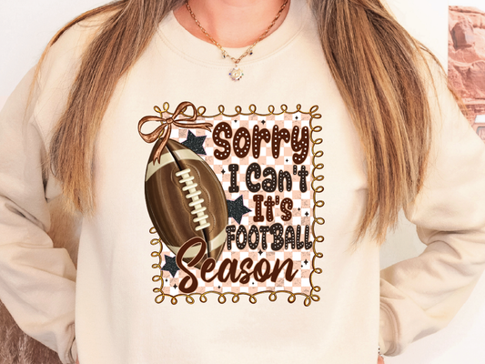 A person wearing a white sweatshirt with a graphic design featuring a football and the text "Sorry I Can't It's Football Season" printed on it.