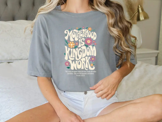 a woman sitting on a bed wearing a t - shirt that says motherhood is