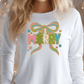 A woman wearing a white long-sleeved shirt with a colorful embroidered design on the front.