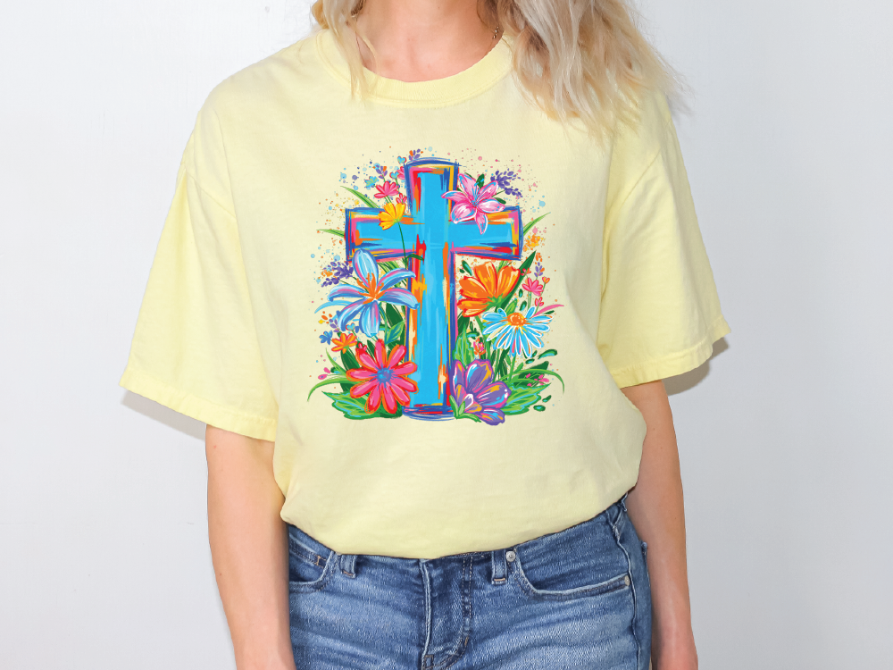 A person wearing a yellow t-shirt with a colorful graphic of a cross surrounded by flowers and foliage.