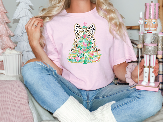 a woman sitting on a bed holding a pink christmas tree t - shirt