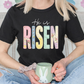 A person wearing a black t-shirt with the text "He is Risen" is holding a green mug with a bunny design.