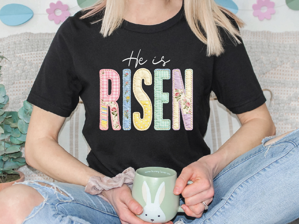 A person wearing a black t-shirt with the text "He is Risen" is holding a green mug with a bunny design.