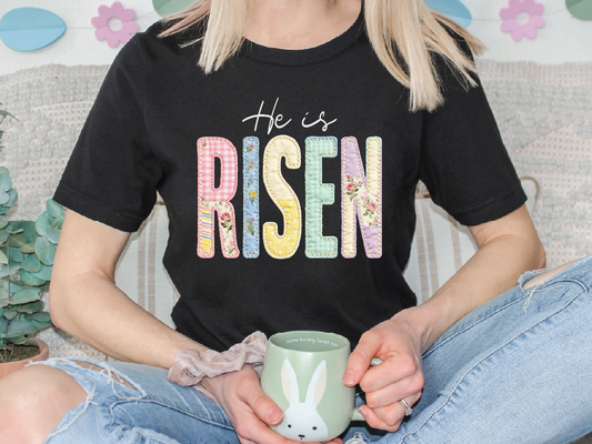 A person wearing a black t-shirt with the text "He is Risen" is holding a green mug with a bunny design.