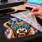 Peeling the clear film away from a freshly pressed DTF transfer on a black t-shirt, the design staying on the fabric