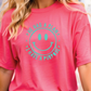 A person wearing a pink t-shirt with a smiley face design and text printed on it.