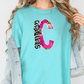 A woman wearing a turquoise t-shirt with a large pink and black letter 'C' printed on it, along with a denim jacket.