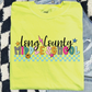 A bright yellow t-shirt with colorful text and graphics, including a smiley face, stars, and checkered patterns, is displayed on a patterned surface.