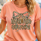 A woman wearing a peach-colored t-shirt with a graphic design featuring a bow and the text "HUMMING SEASON" printed on it.
