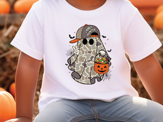 A white t-shirt with a graphic of a ghost character wearing a baseball cap and holding a carved pumpkin, surrounded by Halloween-themed elements.