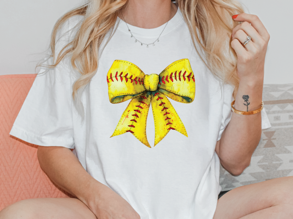 a woman sitting on a couch wearing a softball bow t - shirt