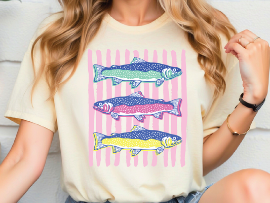 A woman wearing a white t-shirt with a colorful graphic of three fish swimming in a striped pattern.