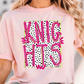 A woman wearing a pink t-shirt with the text "KNIGHTS" printed on it in pink and black.